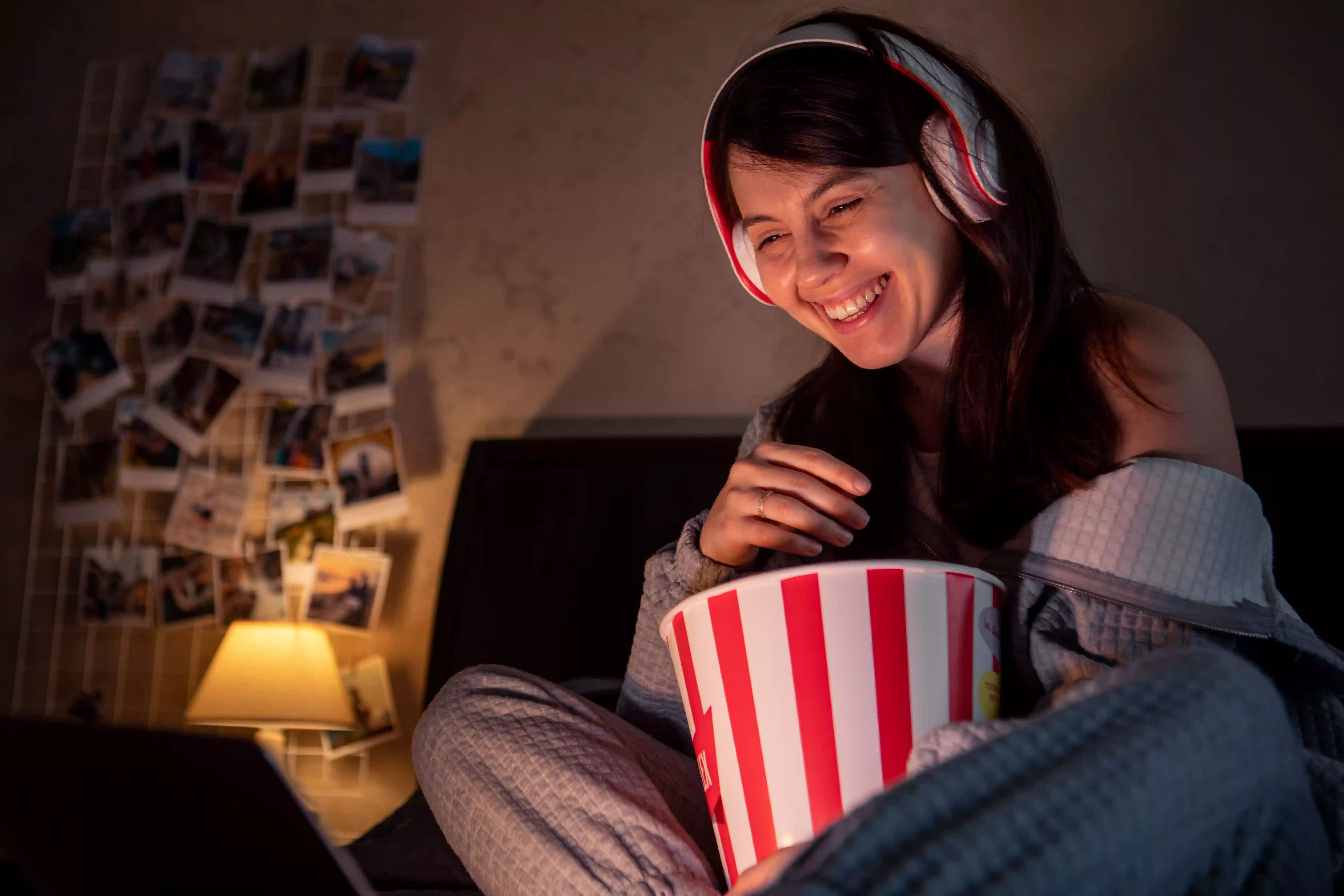 Joven con auriculares en la cama comiendo palomitas de maíz viendo cortos en inglés